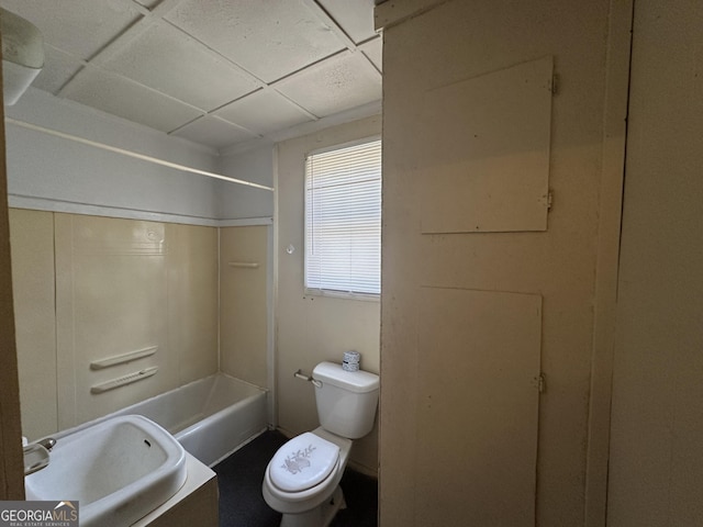 bathroom featuring a drop ceiling, toilet, shower / tub combination, and a sink