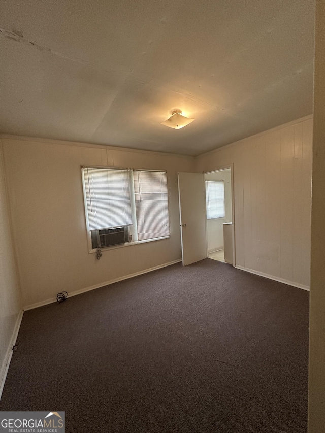 empty room featuring dark colored carpet, cooling unit, and baseboards