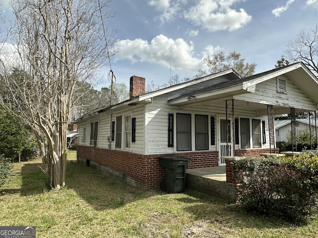 view of side of home featuring a yard, brick siding, covered porch, and a chimney