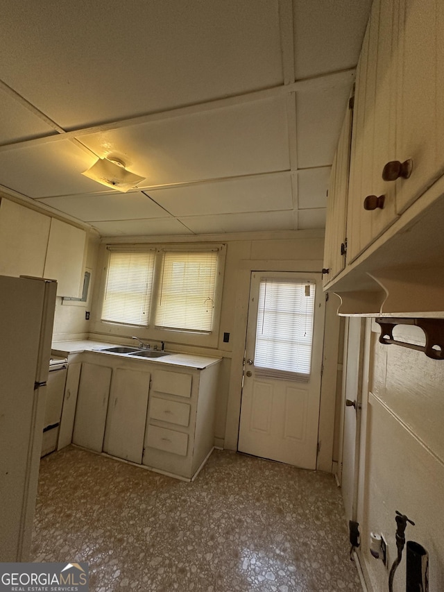 kitchen featuring tile patterned floors, a sink, freestanding refrigerator, white cabinets, and light countertops