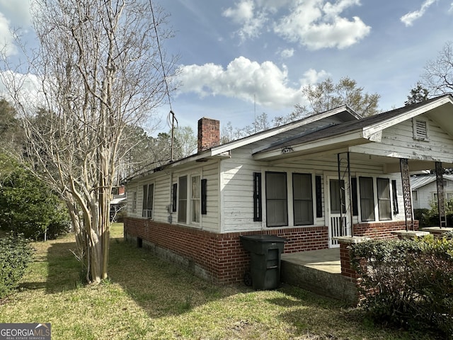 view of side of property featuring brick siding, covered porch, a chimney, and a yard