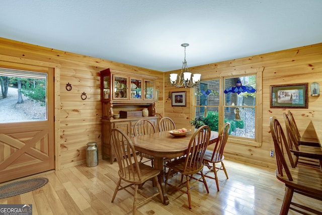 dining space with wooden walls, light wood-type flooring, plenty of natural light, and an inviting chandelier