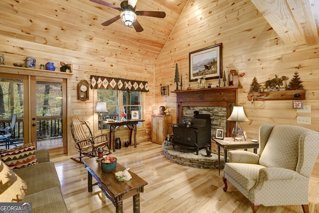 living area with wood finished floors, wooden walls, ceiling fan, a wood stove, and wooden ceiling