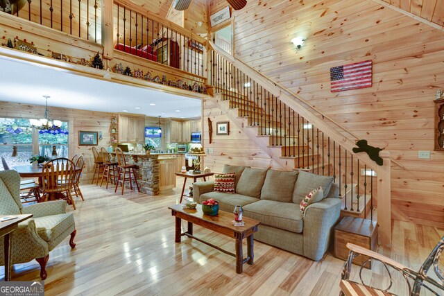 living area featuring a high ceiling, an inviting chandelier, wooden walls, light wood-style flooring, and stairs
