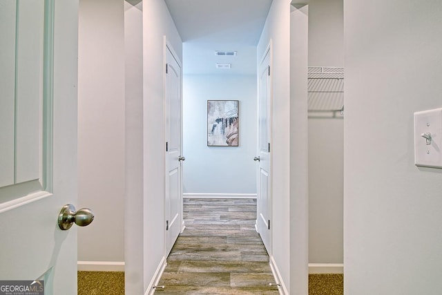 hallway featuring visible vents, baseboards, and wood finished floors