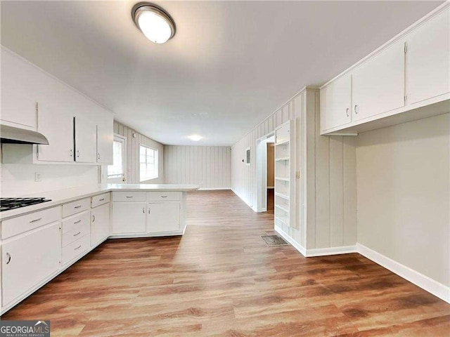 kitchen featuring light countertops, light wood-style flooring, a peninsula, black gas stovetop, and white cabinets