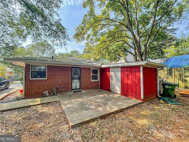 back of house featuring brick siding, an outdoor structure, a storage shed, and a patio area