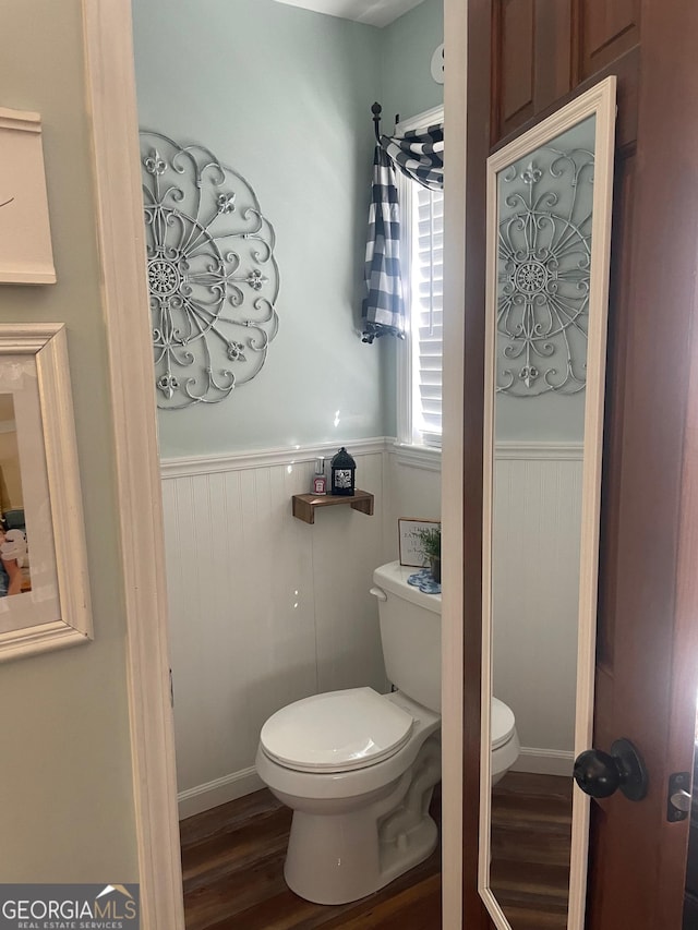 half bath with toilet, wood finished floors, and wainscoting