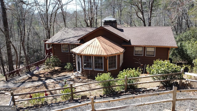 view of side of home with a wooded view, a chimney, roof with shingles, and fence