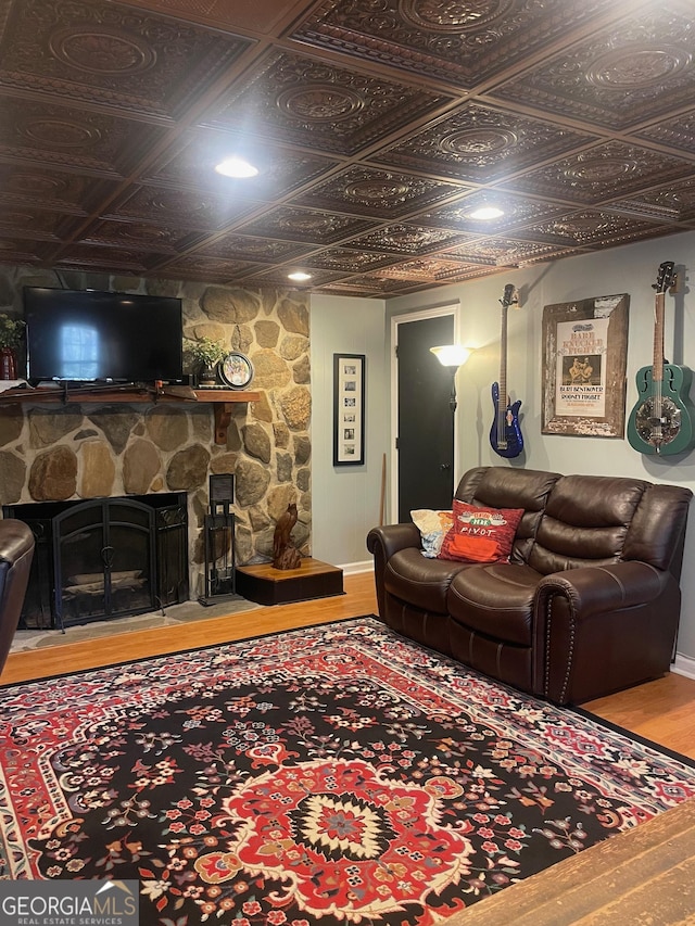 living room with a stone fireplace, wood finished floors, and an ornate ceiling