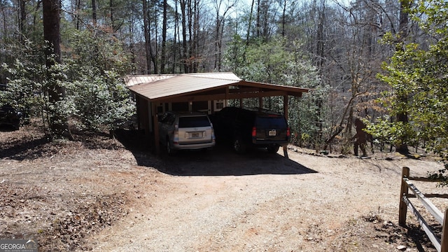 view of car parking featuring a carport, a view of trees, and dirt driveway