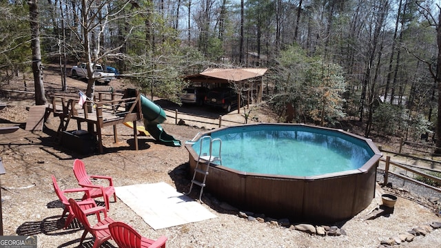 view of swimming pool with a playground and a view of trees