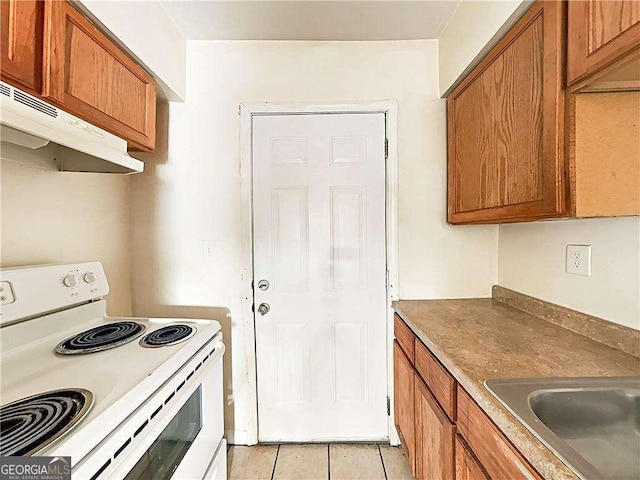 kitchen with under cabinet range hood, a sink, white electric range oven, brown cabinetry, and light tile patterned floors