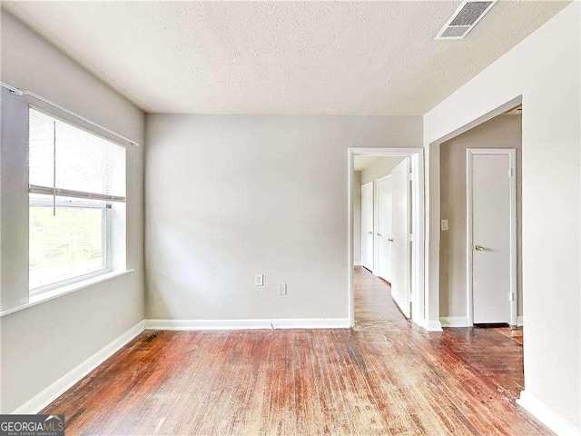 empty room with visible vents, a textured ceiling, baseboards, and wood finished floors