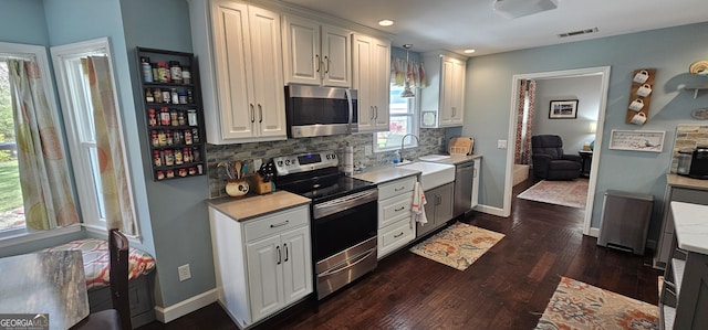 kitchen with a sink, light countertops, decorative backsplash, appliances with stainless steel finishes, and dark wood-style flooring