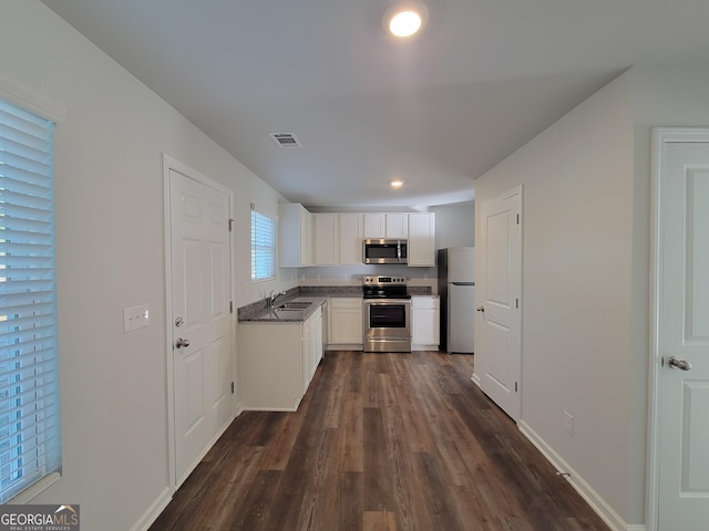 kitchen with dark countertops, visible vents, appliances with stainless steel finishes, white cabinets, and a sink