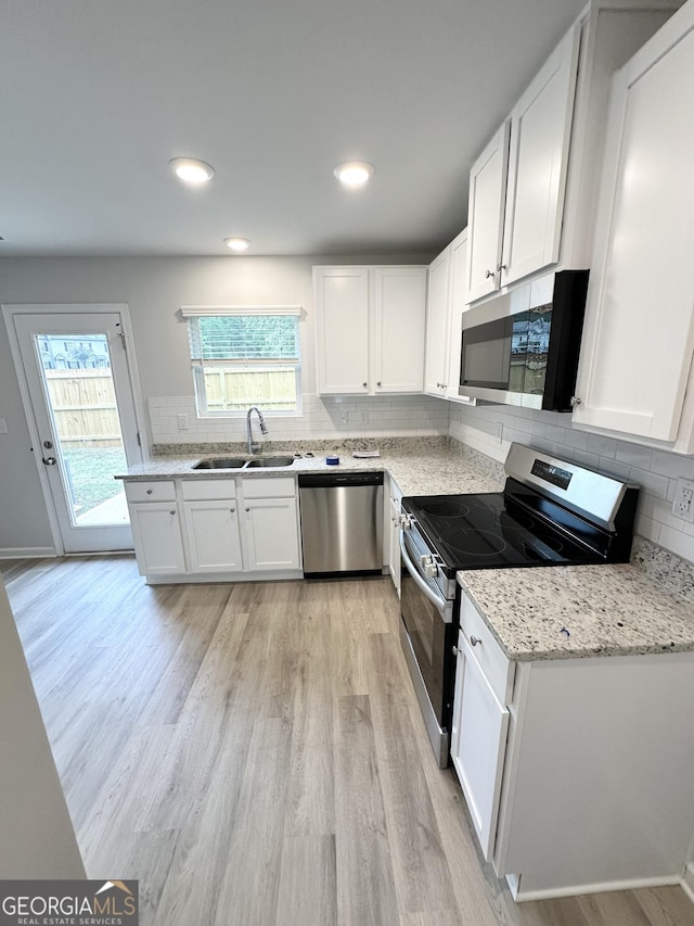 kitchen with light wood finished floors, a sink, stainless steel appliances, white cabinetry, and tasteful backsplash