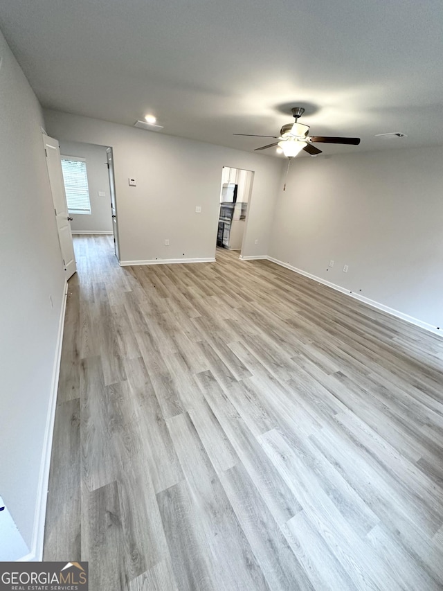 unfurnished living room featuring light wood-style flooring, baseboards, and a ceiling fan