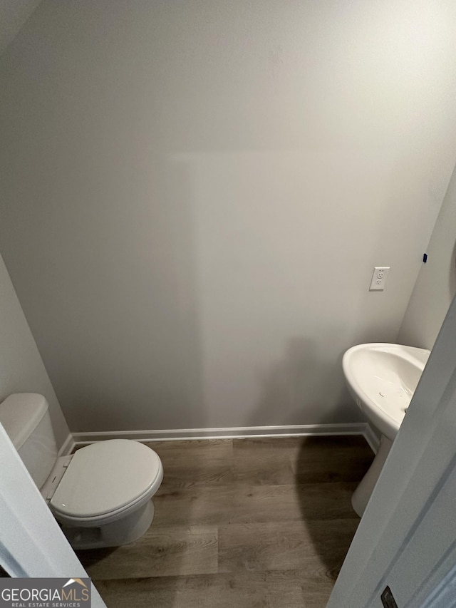 half bathroom with toilet, baseboards, and wood finished floors