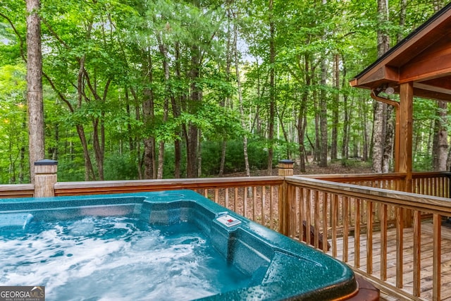 view of pool featuring a deck, a forest view, and a hot tub