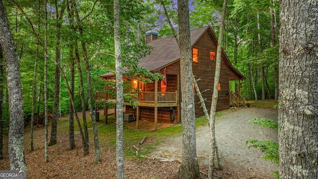 exterior space featuring driveway, central AC, roof with shingles, a wooded view, and a chimney