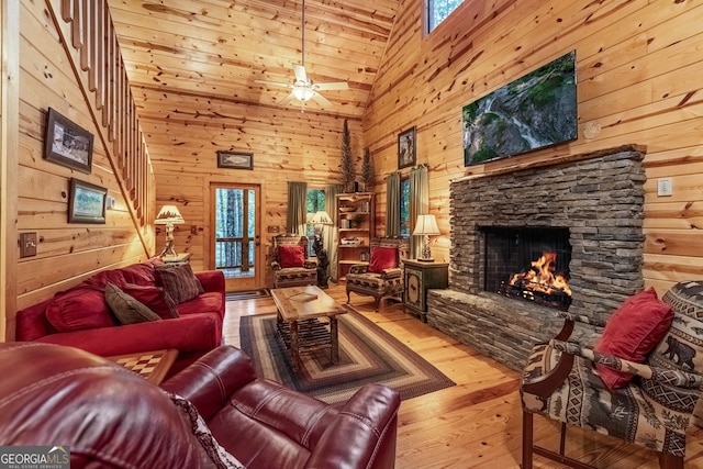 living room featuring hardwood / wood-style floors, wooden walls, a fireplace, and a ceiling fan