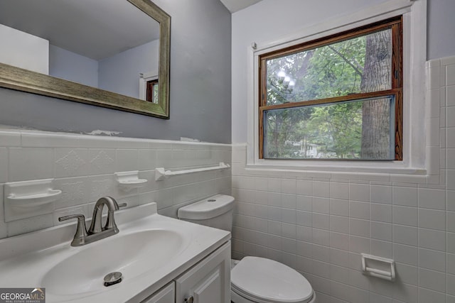 half bath featuring vanity, toilet, tile walls, and wainscoting