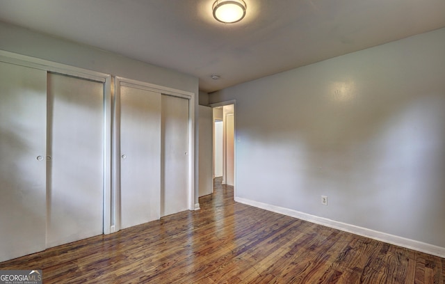 unfurnished bedroom featuring two closets, baseboards, and dark wood finished floors