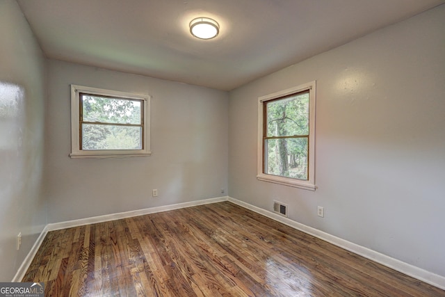 empty room with baseboards, dark wood-style flooring, visible vents, and a healthy amount of sunlight