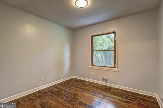 empty room featuring dark wood-type flooring, visible vents, and baseboards