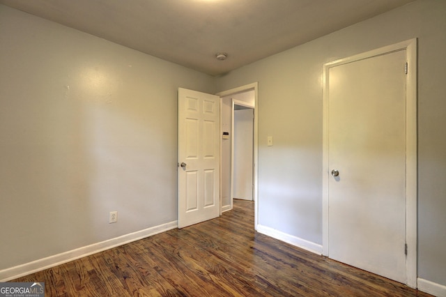 unfurnished bedroom with baseboards and dark wood-type flooring