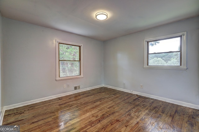 spare room featuring a wealth of natural light, dark wood-type flooring, baseboards, and visible vents