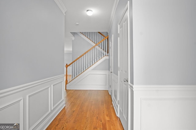 corridor featuring a decorative wall, stairway, light wood-type flooring, and ornamental molding