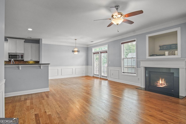 unfurnished living room with a glass covered fireplace, light wood-style flooring, ceiling fan, and ornamental molding