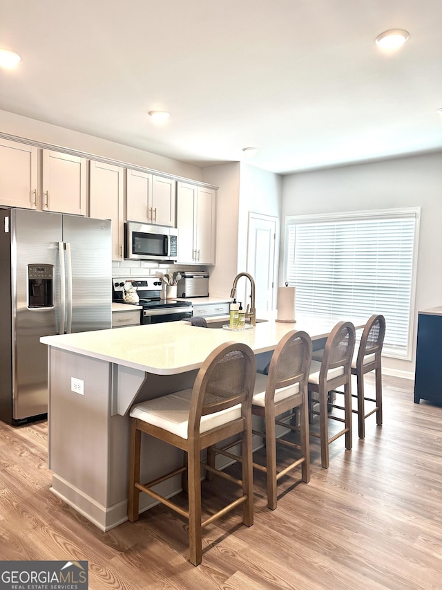 kitchen with a breakfast bar, stainless steel appliances, decorative backsplash, light countertops, and light wood-type flooring