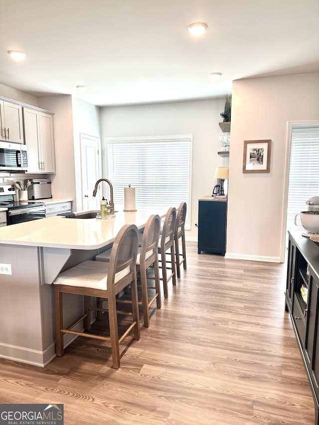 kitchen with a breakfast bar, light wood-type flooring, light countertops, stainless steel appliances, and a sink