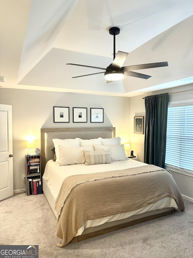 carpeted bedroom with visible vents, baseboards, a raised ceiling, and a ceiling fan