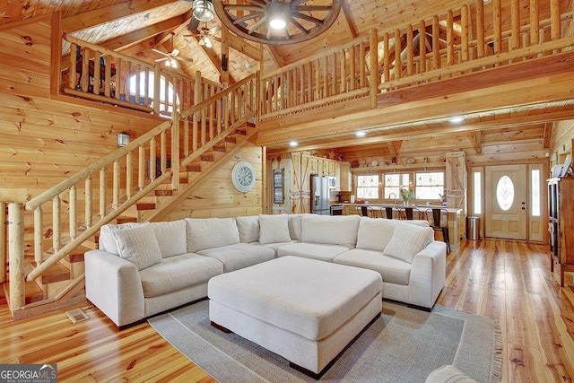 living area with wooden walls, light wood-style flooring, stairs, and ceiling fan