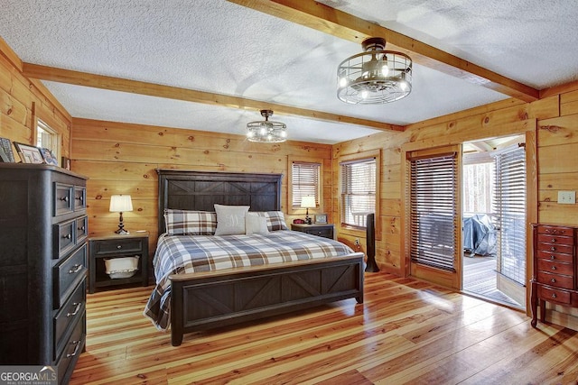 bedroom with beam ceiling, light wood-style flooring, access to exterior, wood walls, and a textured ceiling