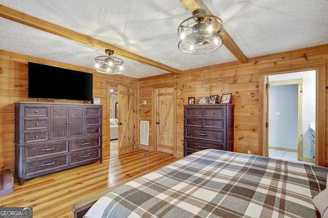 bedroom with beamed ceiling, wooden walls, visible vents, and a textured ceiling