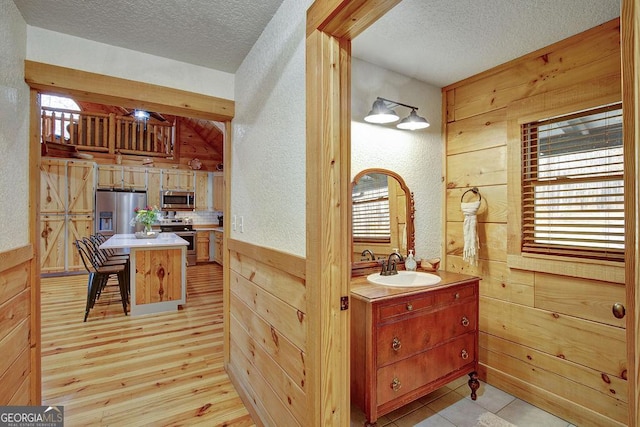 bathroom featuring wooden walls, a textured ceiling, a wainscoted wall, and wood finished floors