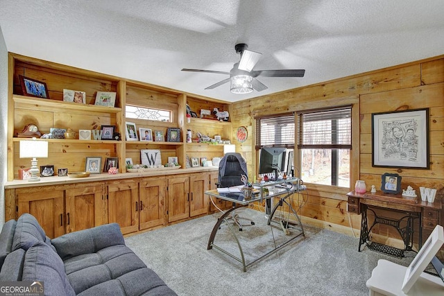 office with light colored carpet, wooden walls, a ceiling fan, and a textured ceiling