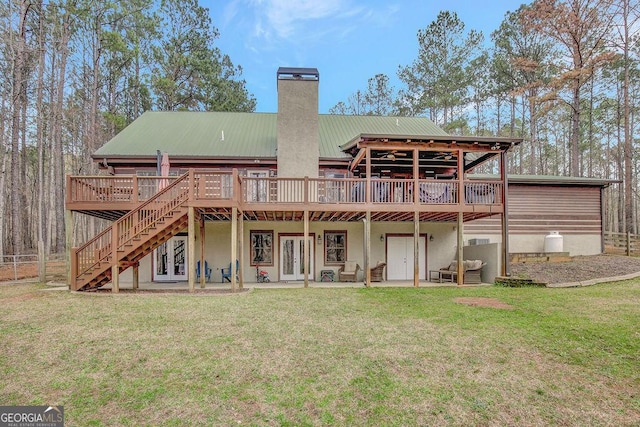 back of house with a wooden deck, a chimney, french doors, a lawn, and metal roof