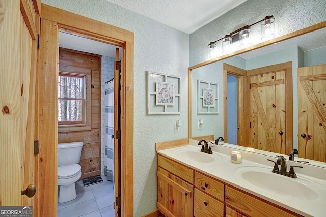 bathroom with tile patterned flooring, toilet, a textured wall, and a sink