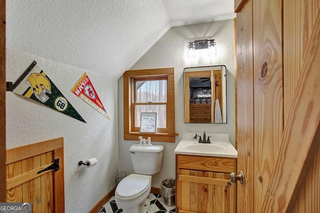 half bathroom featuring toilet, a textured ceiling, vaulted ceiling, vanity, and a textured wall