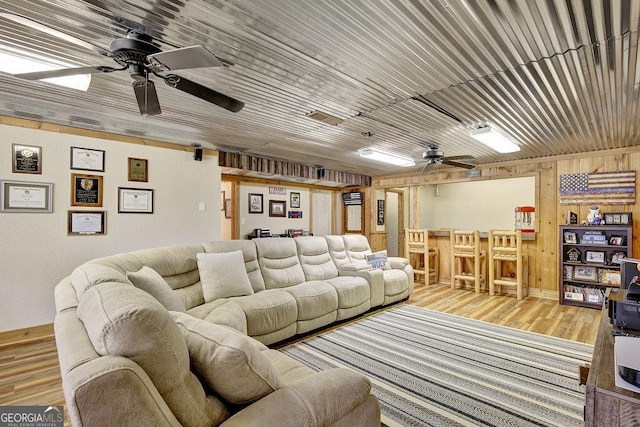 living area featuring visible vents, wooden walls, wood finished floors, and a ceiling fan