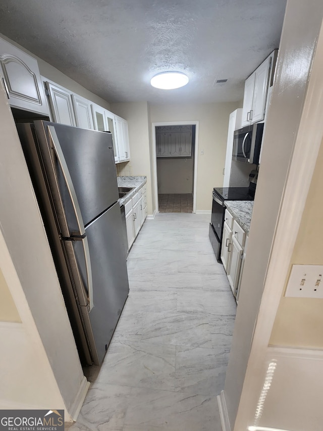 kitchen with marble finish floor, a textured ceiling, stainless steel appliances, white cabinets, and baseboards