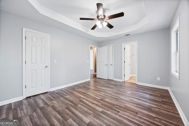 unfurnished bedroom featuring wood finished floors, a tray ceiling, and visible vents