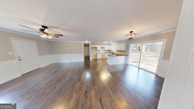 unfurnished living room with dark wood finished floors, crown molding, a ceiling fan, and wainscoting