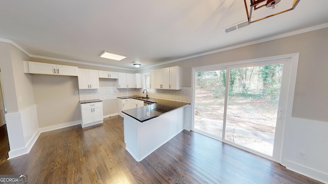 kitchen featuring dark countertops, a peninsula, tasteful backsplash, and a sink